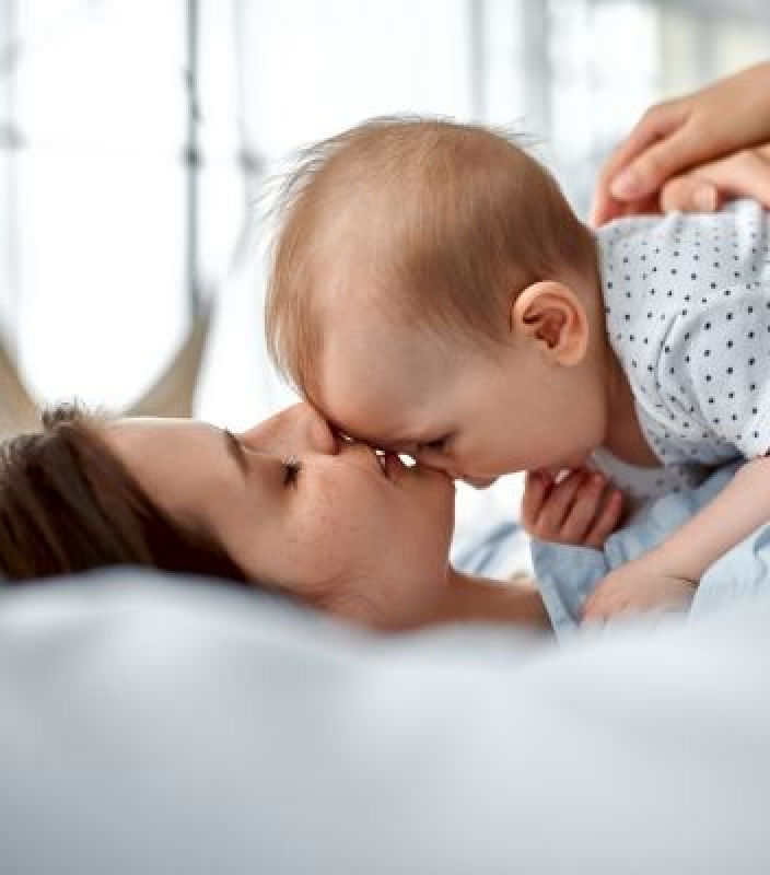 茶髪の母親が仰向けに寝たまま、赤ちゃんを抱き、額にキスをしています。   -  ヒョンデモビリティジャパン ブランドストーリー